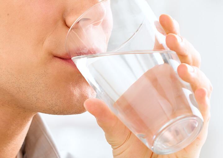 Person trinkt Wasser aus einem klaren Glas.