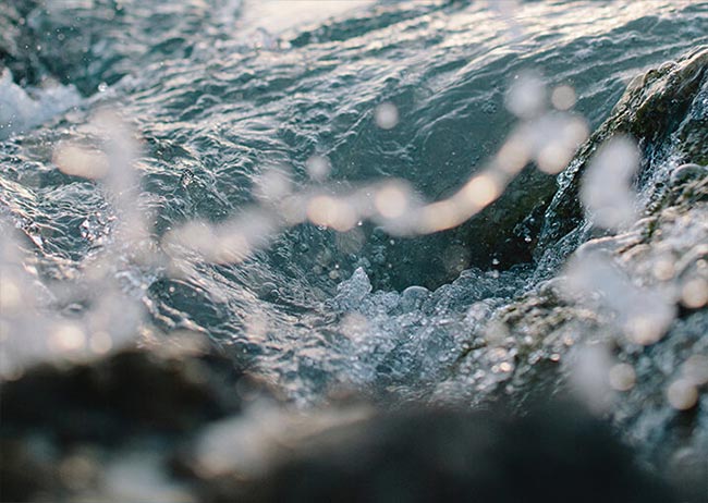 Wellen spritzen über Felsen im Meer, mit schimmerndem Wasser und sprudelndem Schaum im Sonnenlicht.