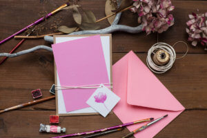 Blank pink wedding invitation or greeting card with art supplies laying around the table.