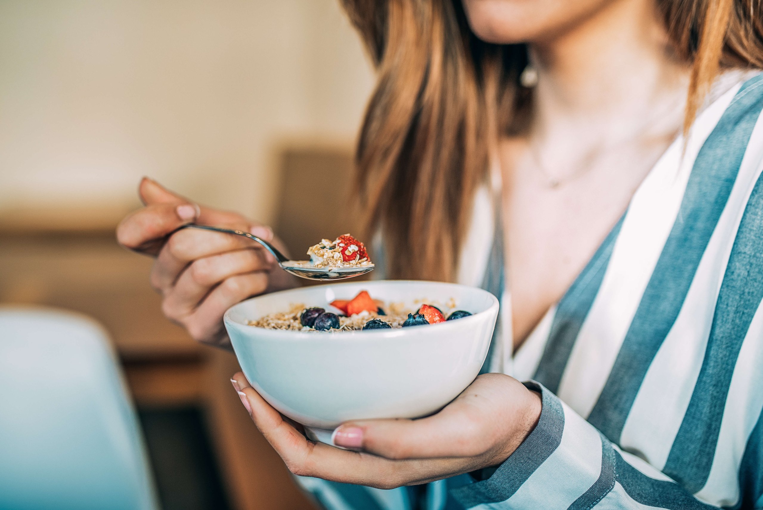 Crop woman close up eating oat and fruits bowl for breakfast