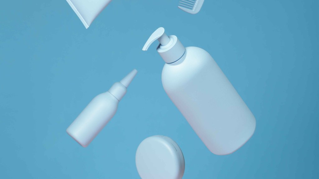 Weiße Kosmetikflaschen und ein Kamm schweben vor blauem Hintergrund.