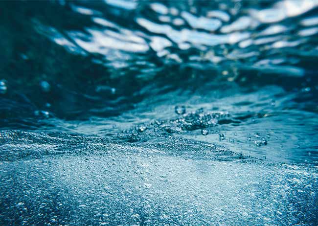 Unterwasseraufnahme mit blauen Wellen und Luftblasen, die nach oben steigen.