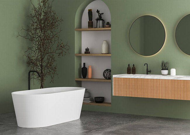 Freistehende weiße Badewanne vor grüner Wand mit Regal, zwei runde Spiegel über Holzwaschbecken.