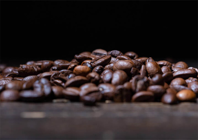 Ein Haufen brauner Kaffeebohnen liegt auf einer dunklen Oberfläche.