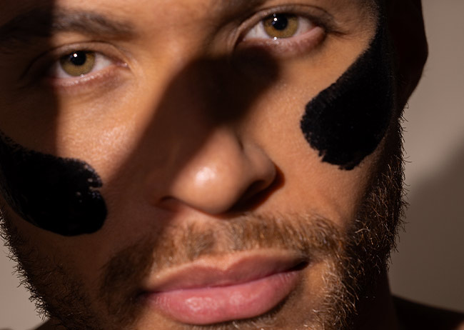 Nahaufnahme eines Gesichts mit schwarzer Aktivkohle Creme Masken Streifen auf den Wangen und Schatten über den Augen.