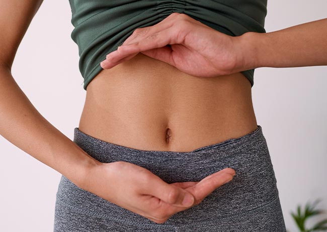 Person in Sportkleidung zeigt mit Händen auf den Bauch.