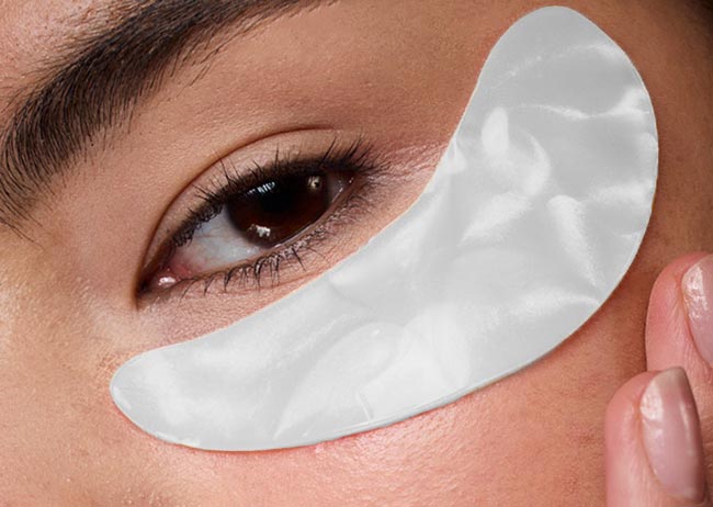 Nahaufnahme eines Auges mit einem weißen Augen Gel Pad darunter. Eine Hand berührt sanft das Gesicht.