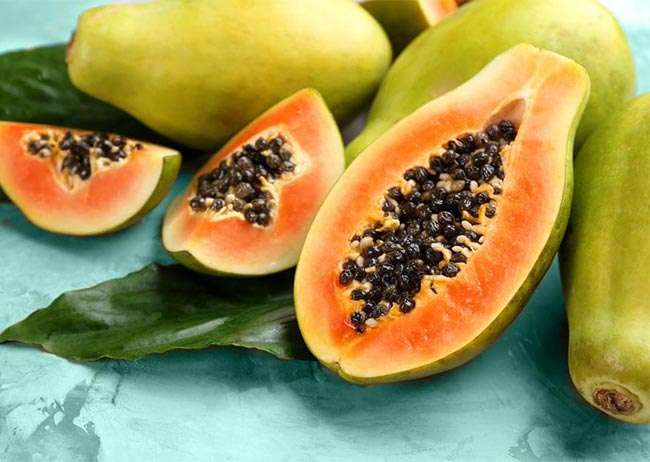 Aufgeschnittene Papayas auf einem grünen Blatt und blauem Hintergrund.