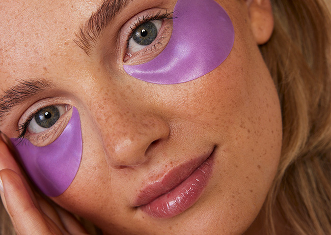 Frau mit lila Augenpads unter den Augen, nahes Gesichtsporträt.