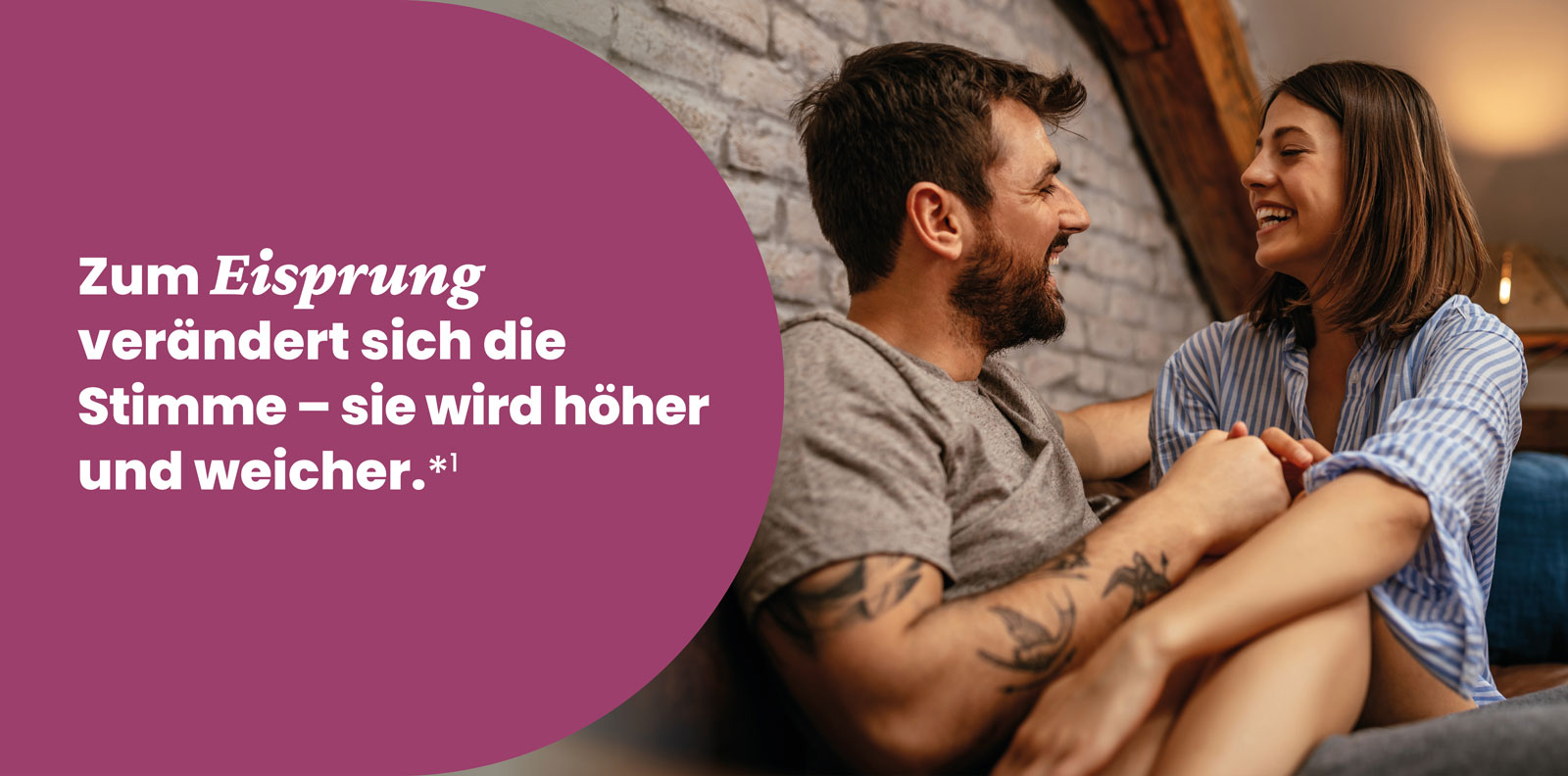 Paar sitzt lächelnd auf Sofa, er mit Bart, sie in gestreiftem Hemd, vor Backsteinwand. Links Text über Eisprung.