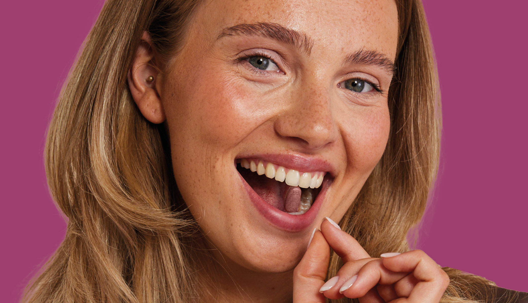 Zyclus Balance Anwendung Eine lächelnde Person mit blonden Haaren vor einem lila Hintergrund, mit offenem Mund und Kapsel zwischen den Zähnen