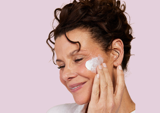 Das Model verreibt auf der linken Wangen das Creme Peeling.